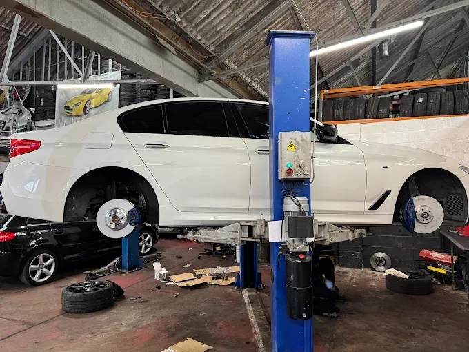 White car on a ramp with wheels removed for brake work at Kam Autos in Derby